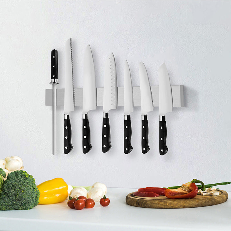 Set of knives on a magnetic knife holder with vegetables on a white surface
